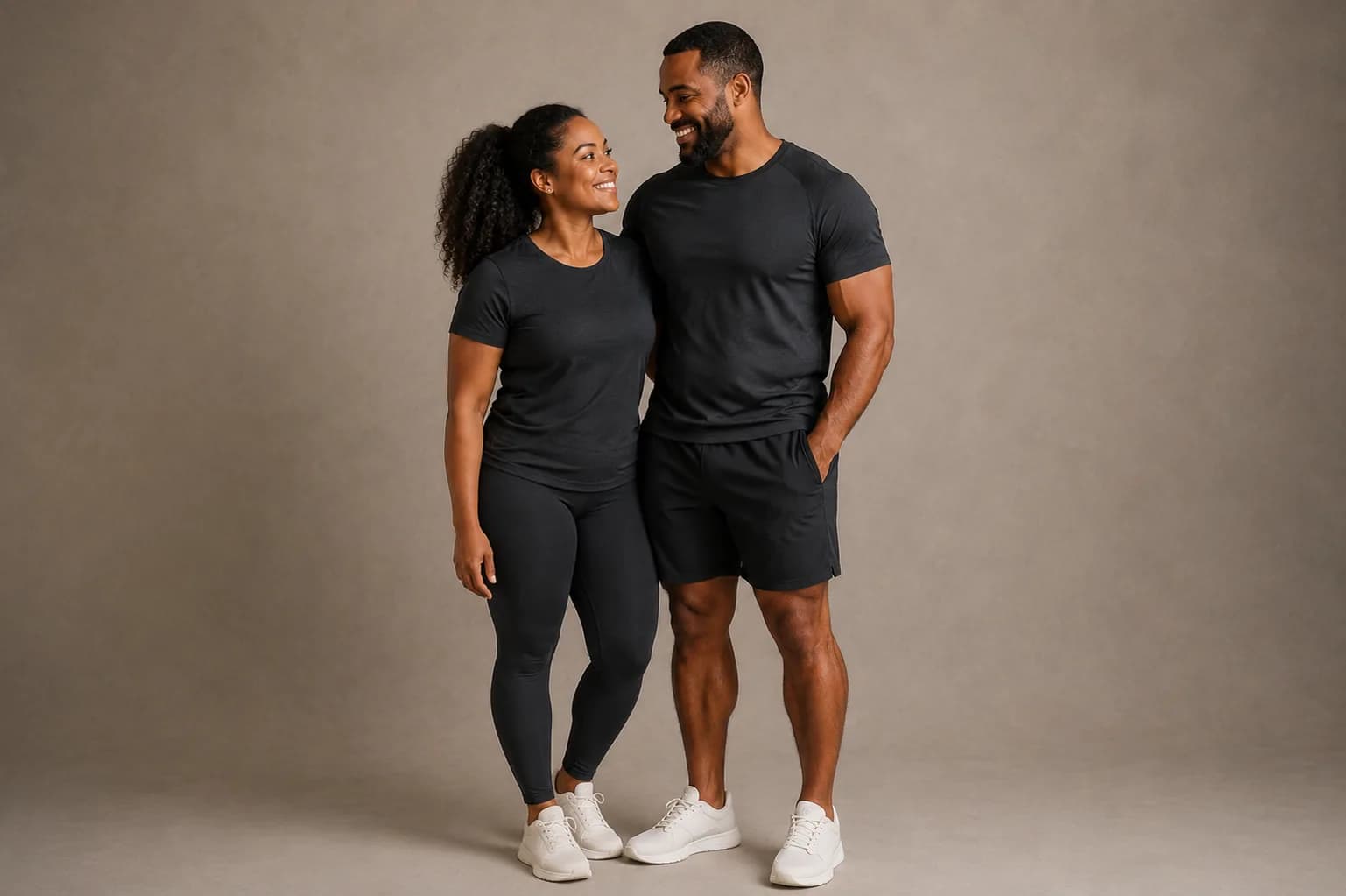 Two people in dark athletic wear standing together against a neutral studio wall