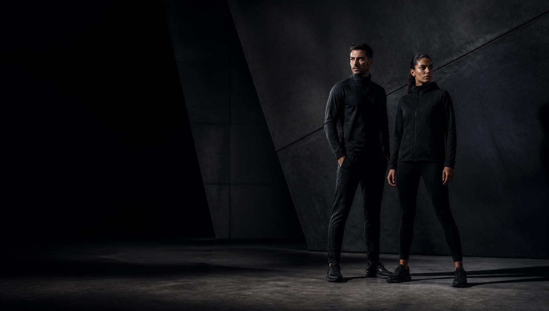 An athletic man and woman in black performance apparel in a dark architectural space